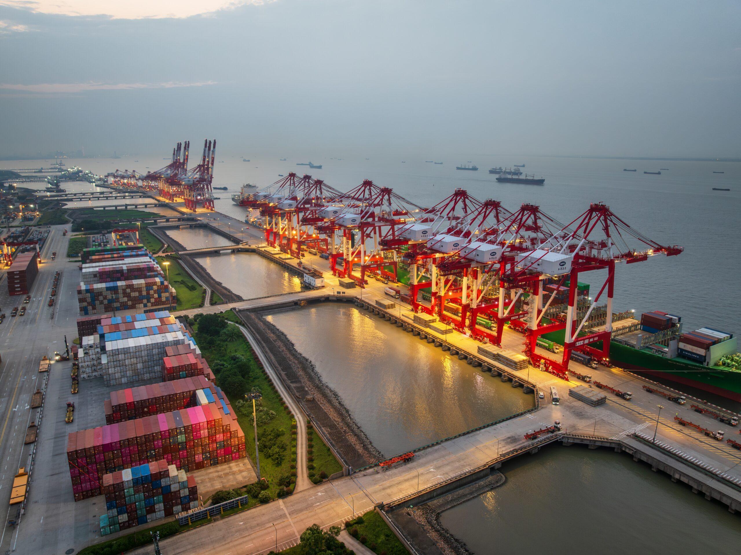 Aerial view of a busy container port with cargo ships, shipping containers, and gantry cranes supporting international ocean freight and global trade.